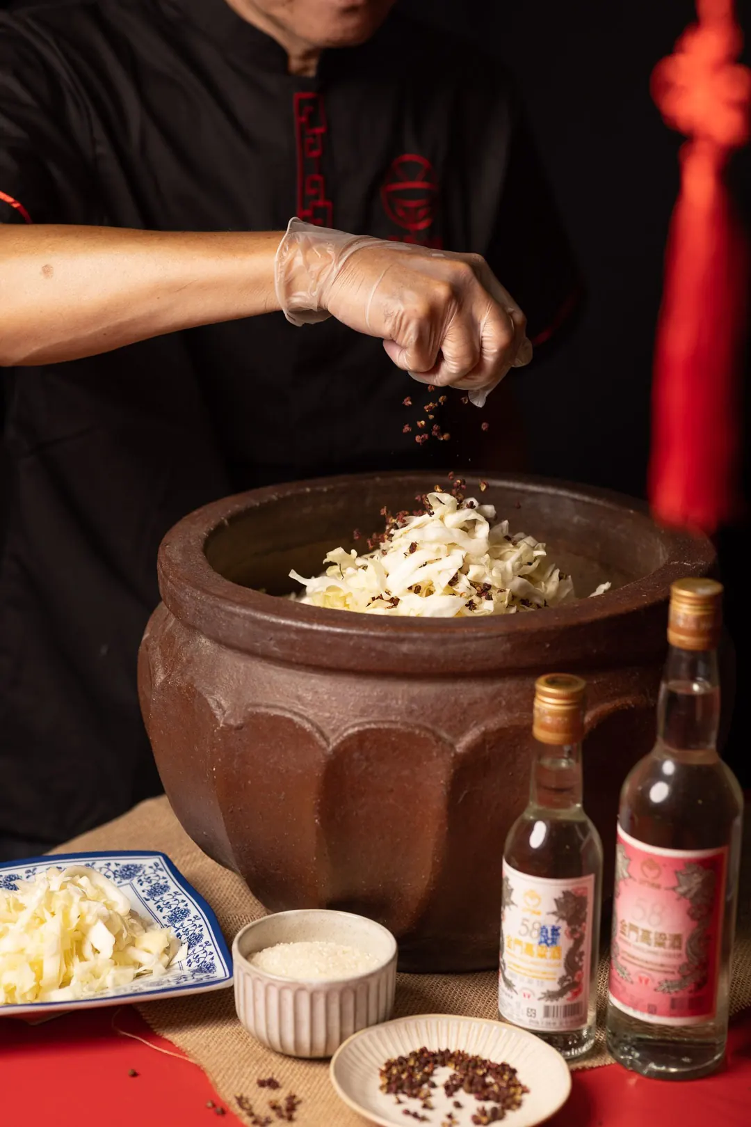 師傅把花椒撒進大缸,一層層醃酸菜,桌上擺著金門高粱酒